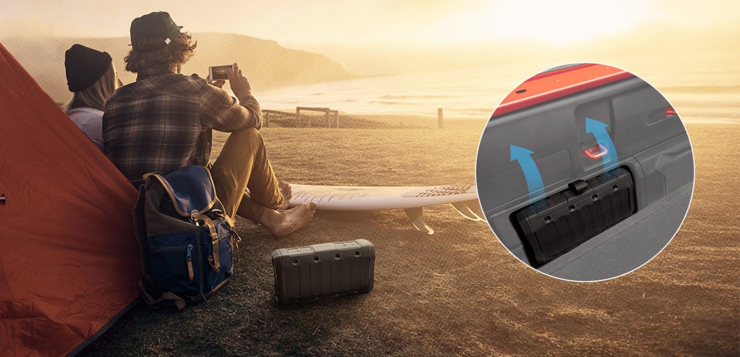The available Bluetooth speaker on a sandy beach with an inset image showing its location in the bed of the 2021 Jeep Gladiator.