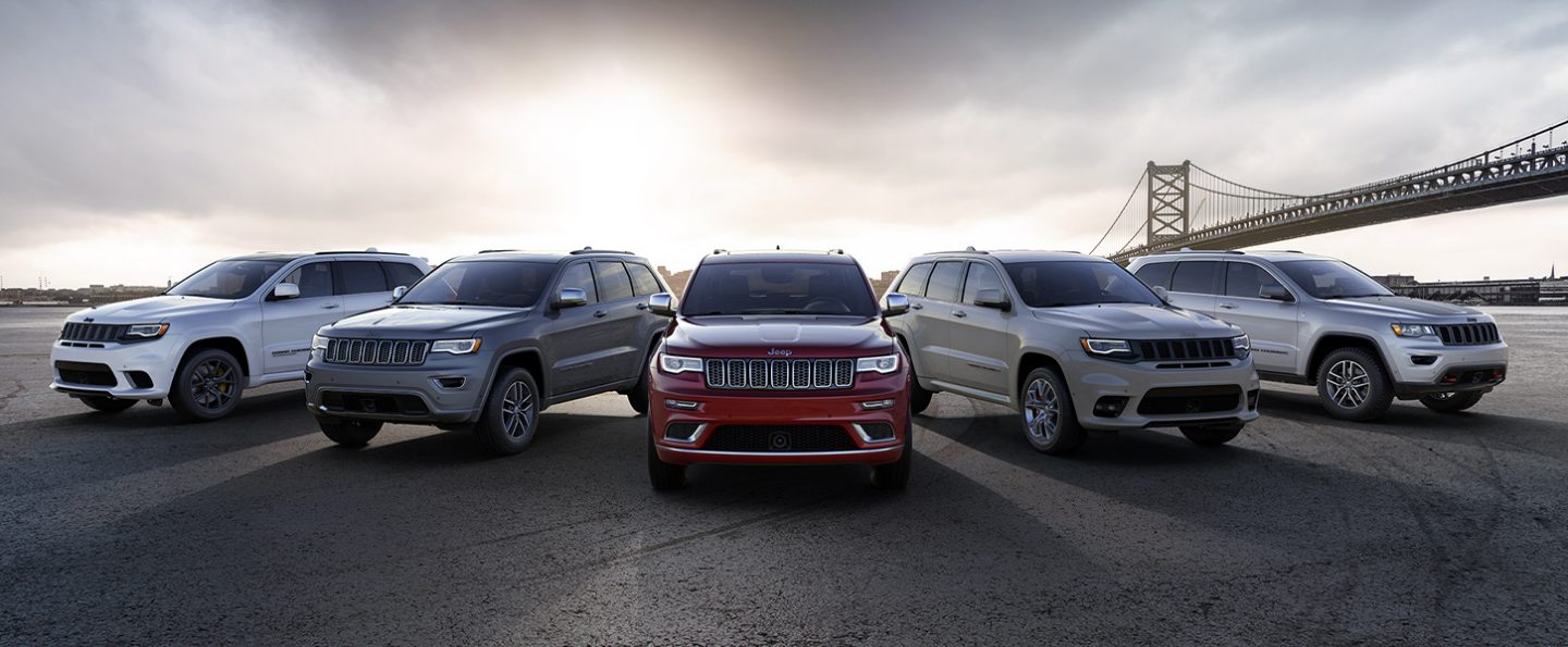 A lineup of five 2021 Jeep Grand Cherokee models with different trim levels parked near a bridge.