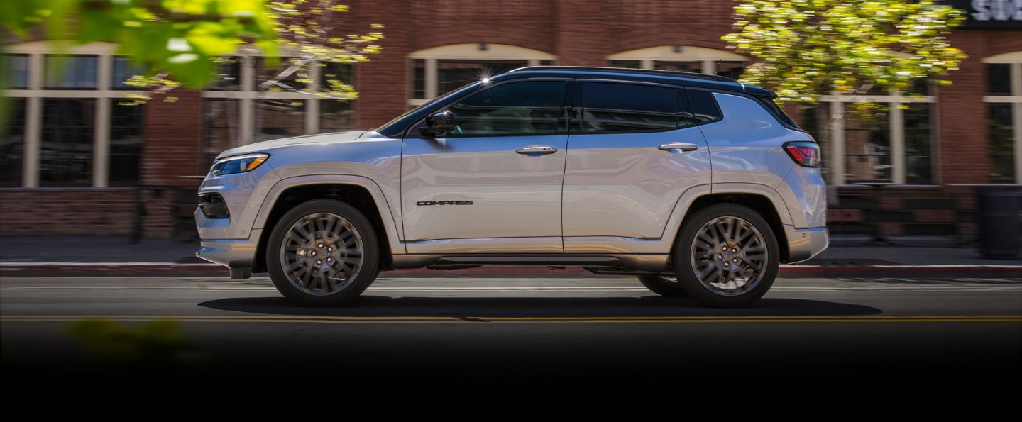 The 2022 Jeep Compass High Altitude being driven down a street past a row of brick buildings.