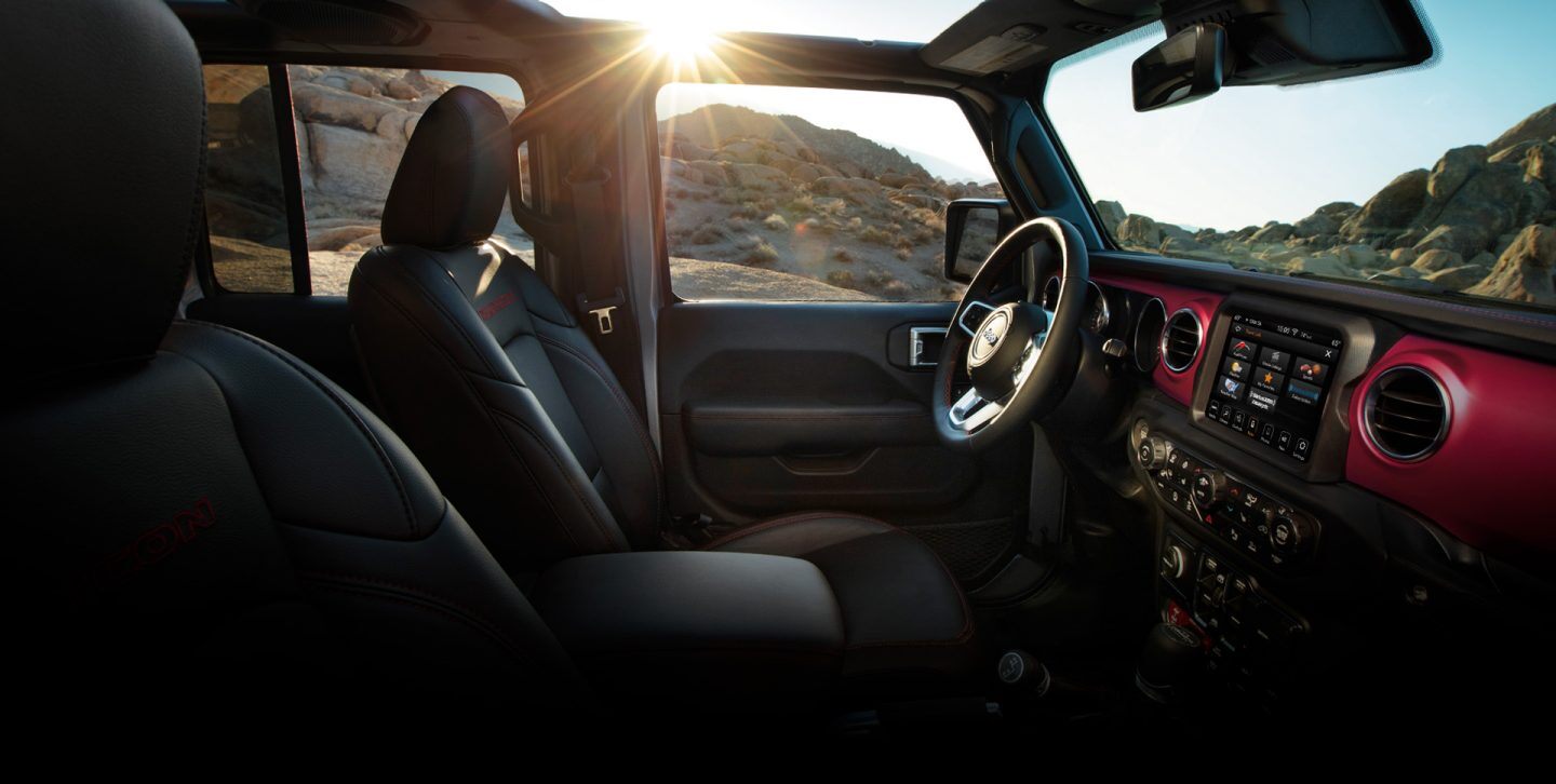 The interior of the 2022 Jeep Gladiator Rubicon with its top off, focusing on the front seats, steering wheel and dash.